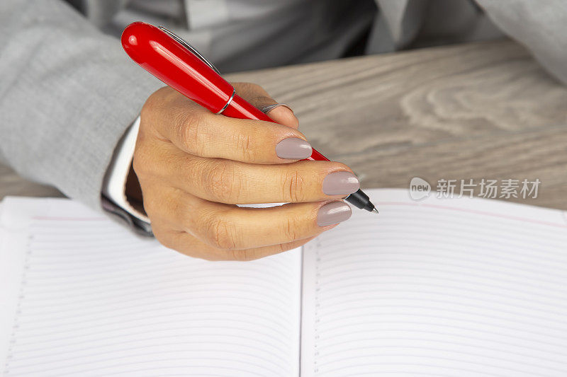 一位女商人的手拿着一支红笔在笔记本的背景上。