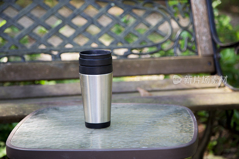 一个可重复使用的咖啡杯放在公园的桌子上。长椅上的背景。