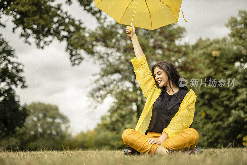 美丽的年轻女子穿着黄色雨衣，拿着黄色雨伞在户外