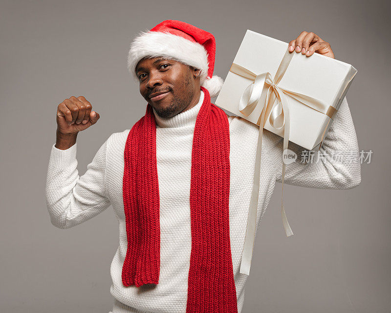 一个皮肤黝黑的年轻人，穿着羊毛衫，戴着圣诞帽，围着鲜红的围巾