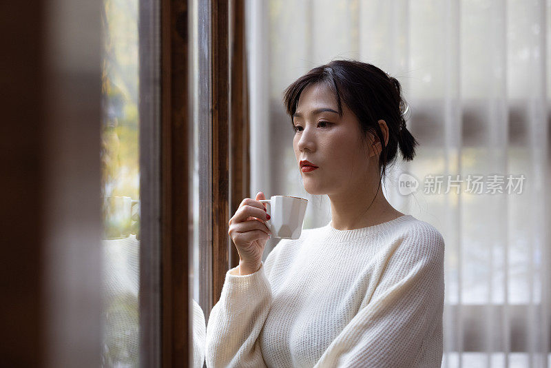 亚洲年轻女子在窗边喝咖啡