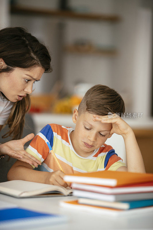 母亲在家里帮助儿子做家庭作业。库存图片