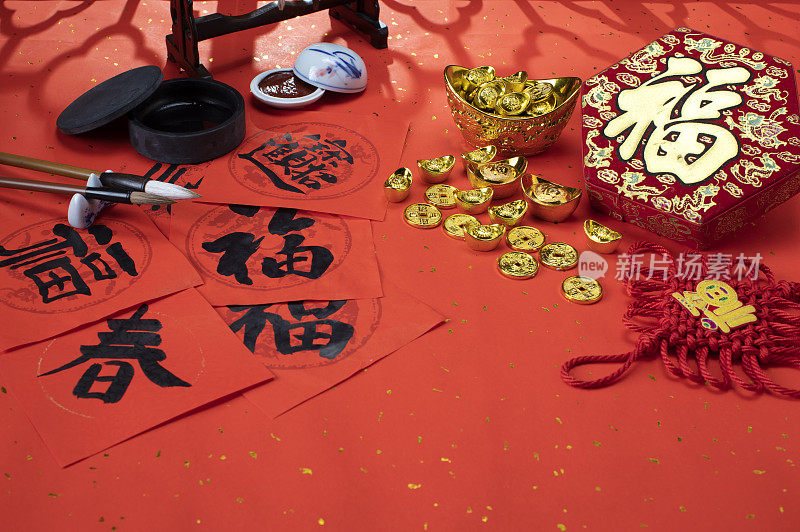 阳光透过窗花照射在中国春节春联并摆放着春字福字及吊饰和金元宝金币和毛笔砚台