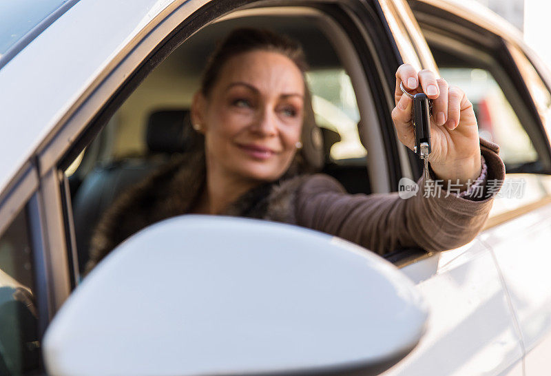 快乐的女人透过窗户炫耀她的新车钥匙