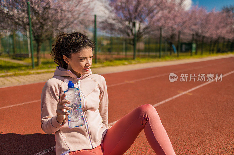 运动的年轻女子在运动轨道上跑步后喝水。