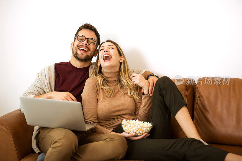 微笑的夫妇在家里放松，在笔记本电脑上看电影