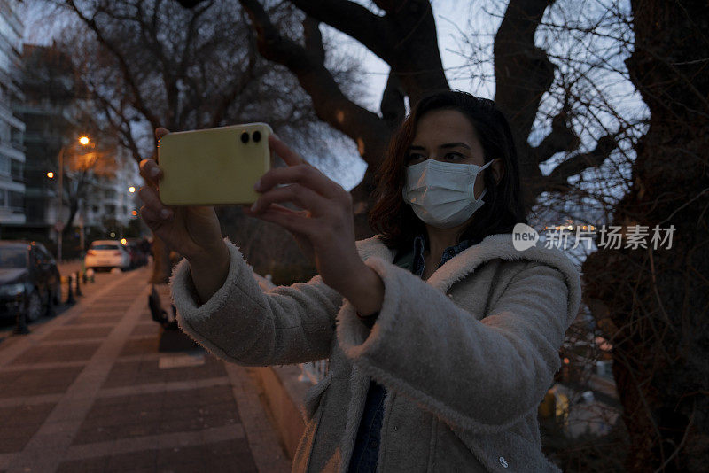 女性游客在城市夜间佩戴防护口罩并使用智能手机