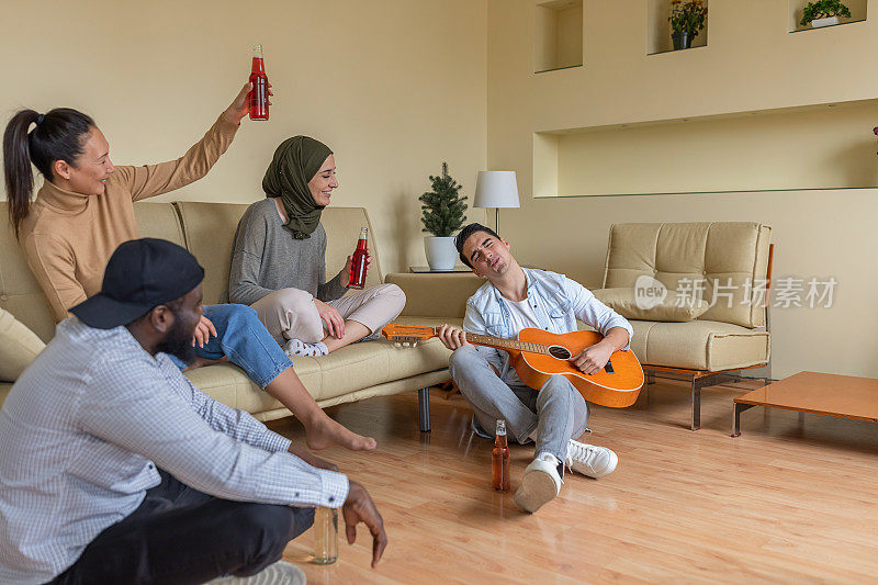 一群快乐的多元文化的年轻朋友正在享受吉他的声音和清爽的饮料。