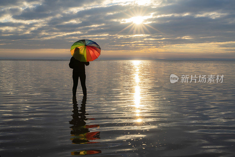 女人撑着雨伞在盐湖风景中看日落