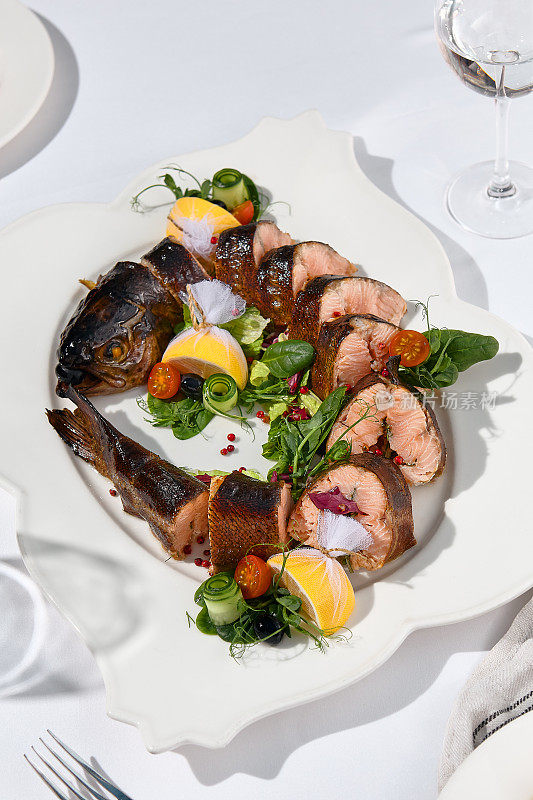 宴会菜肴——白色餐桌上的烟熏虹鳟鱼。优雅的熏鱼鳟鱼晚宴，婚礼，节日派对。宴会菜单的食物造型。