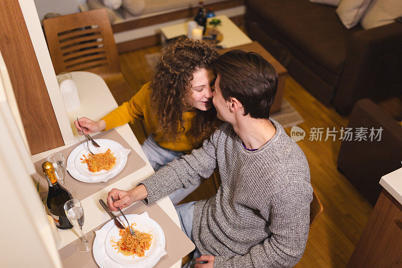 美丽的年轻夫妇在家里喝香槟吃意大利面，享受浪漫的晚餐