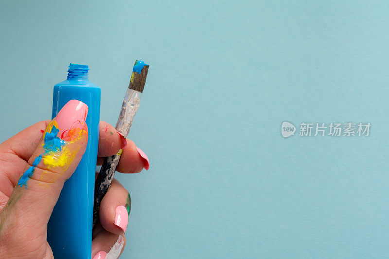 蓝色油漆管与画笔在女性艺术家的手