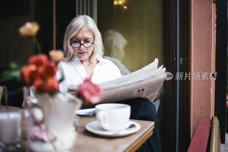 一位高级女士坐在路边咖啡馆里看报纸