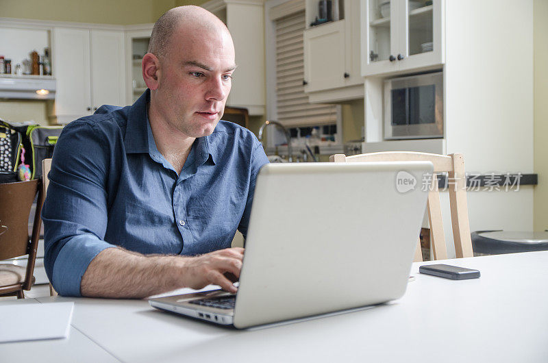 一个秃顶的男人在餐桌上用笔记本电脑工作