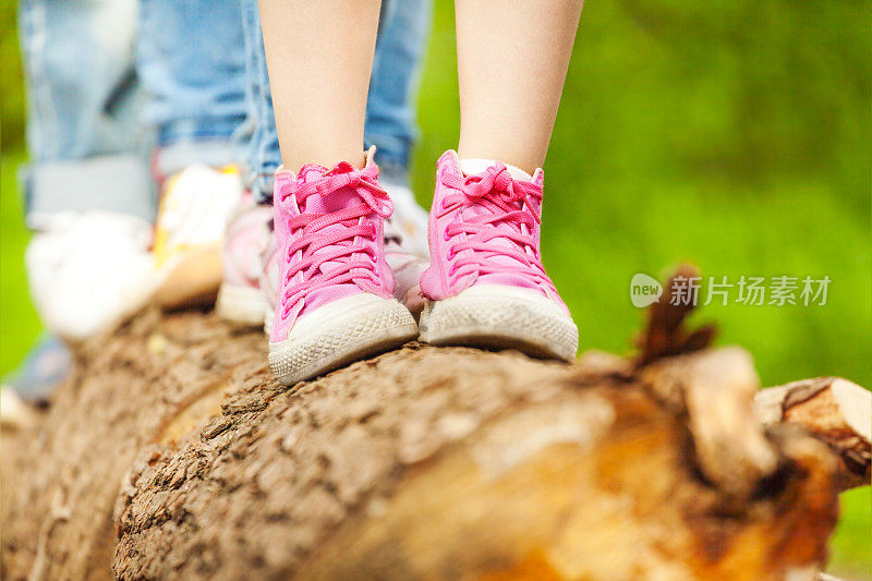 孩子们穿着粉色运动鞋站在一根木头上