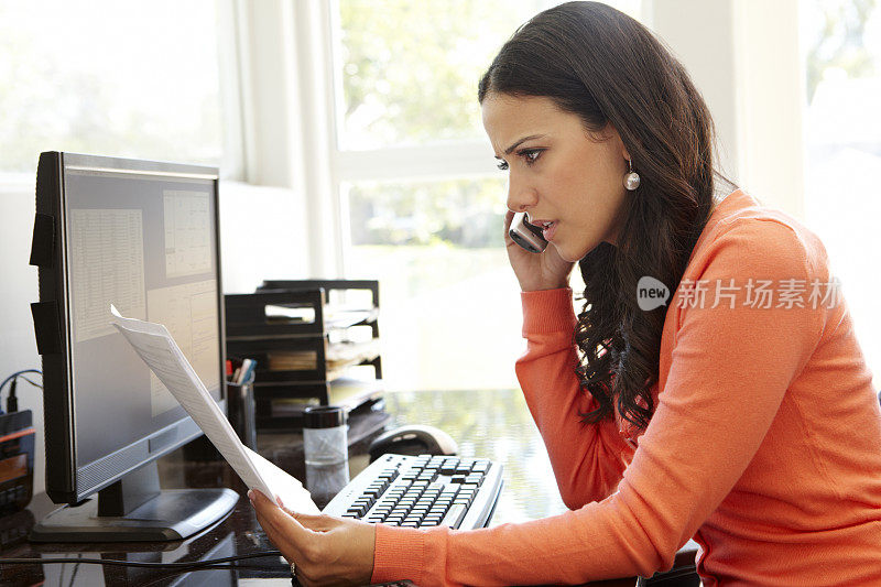 一个西班牙裔女人在电话里拿着家庭办公室的文件