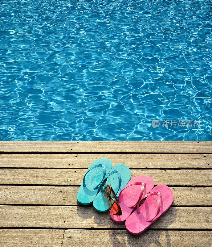 蓝色的泳池边有彩色的拖鞋和太阳镜