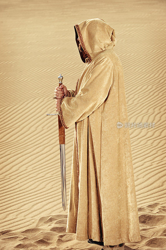 国王在兜帽长袍拿着他的剑-沙背景