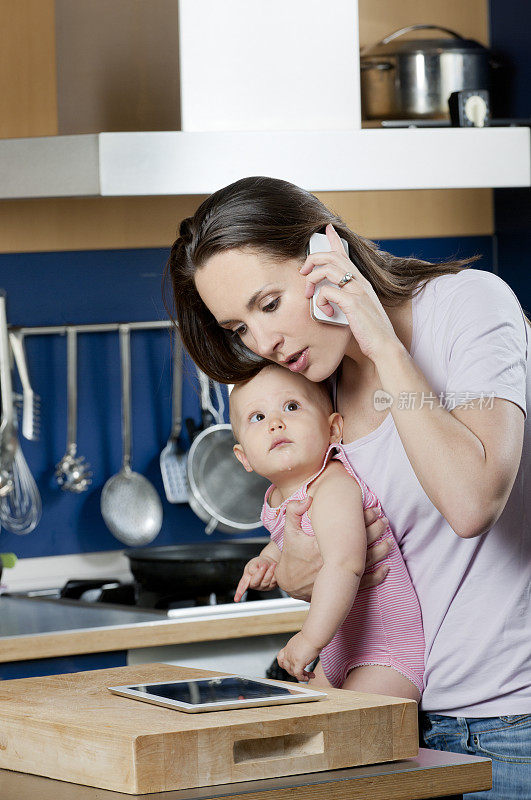 一心多用的女人在厨房里抱着小女孩打电话