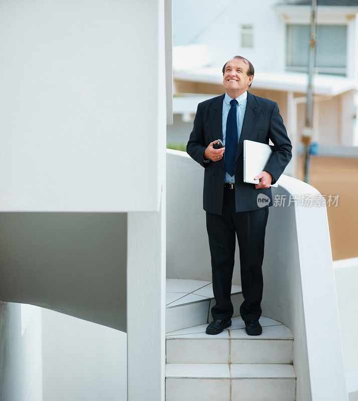 一位高级商务人士在楼梯上拿着笔记本电脑和手机