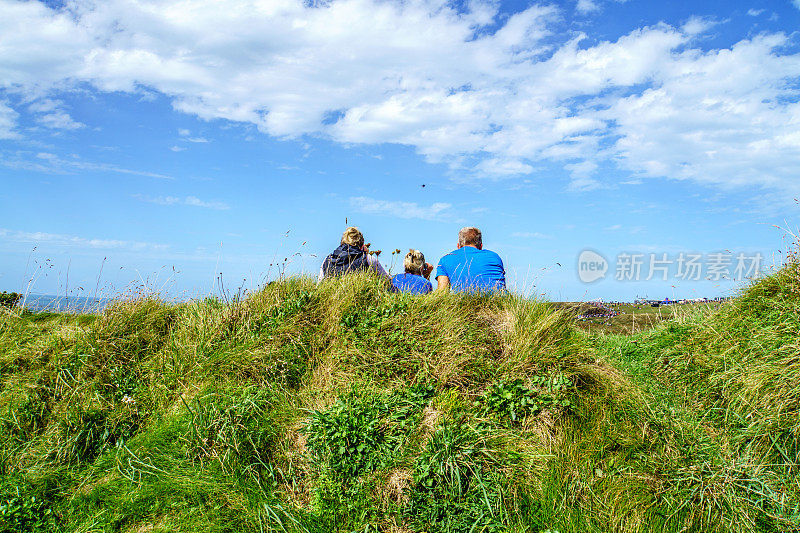 三名摄影师坐在威尔士海岸的草地上