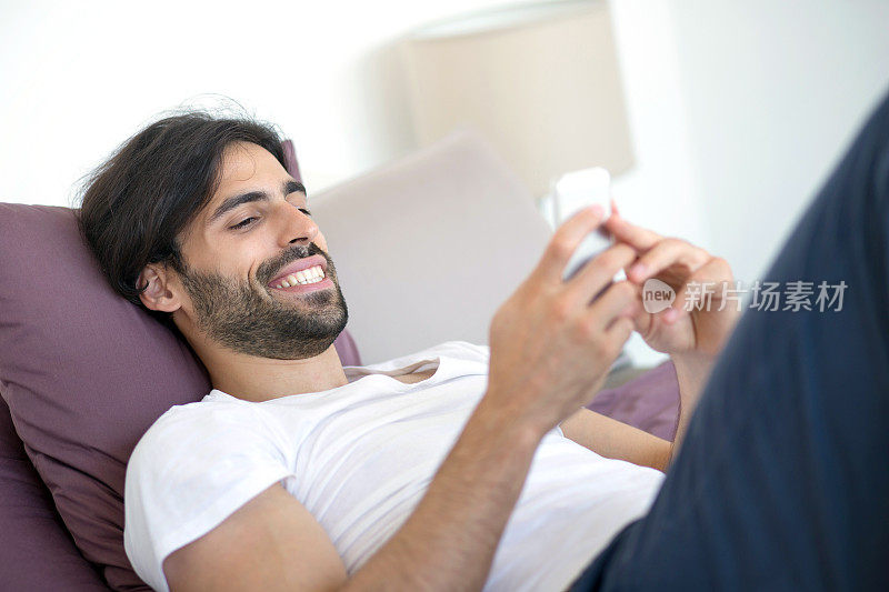 微笑的男人在床上用手机。