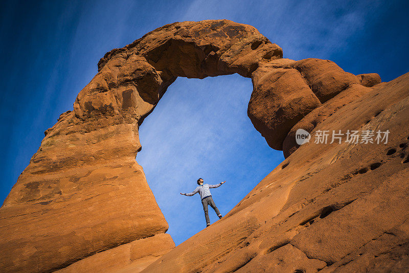 那个快乐的年轻人，徒步旅行者，在夕阳下的精致拱门下感受到了自由。拱门国家纪念碑，犹他州，美国