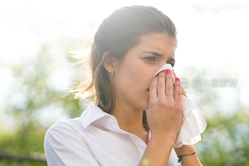 生病的女人在室外用纸巾擤鼻子