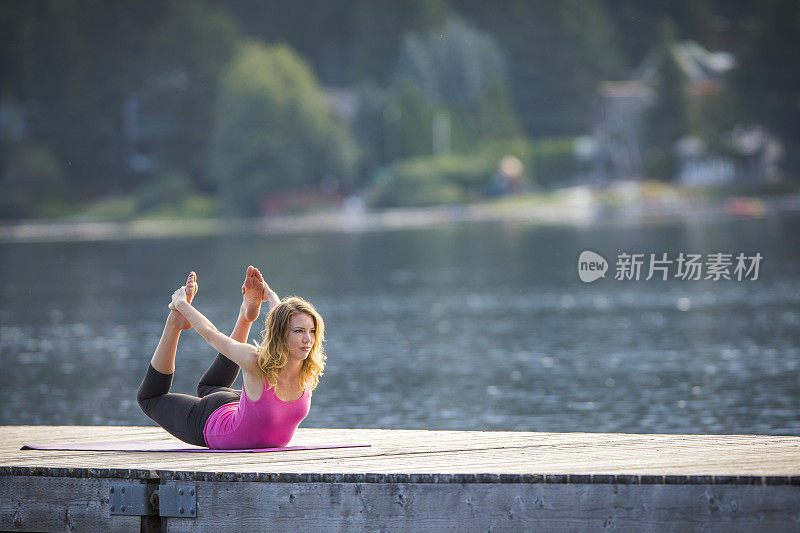 一个年轻女子在湖边的码头上练习瑜伽。