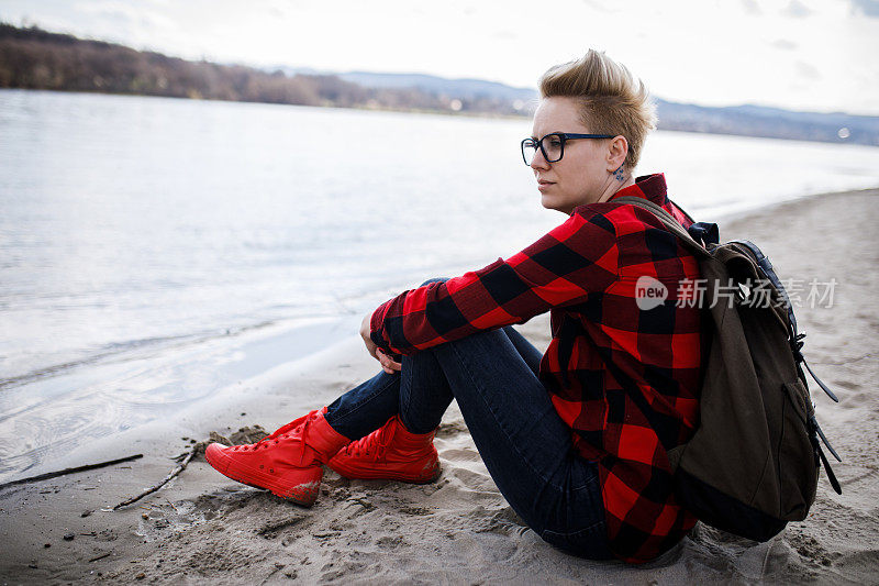 年轻女子坐在湖边的沙滩上。一个独自的旅行者享受自然，风景和她的自由