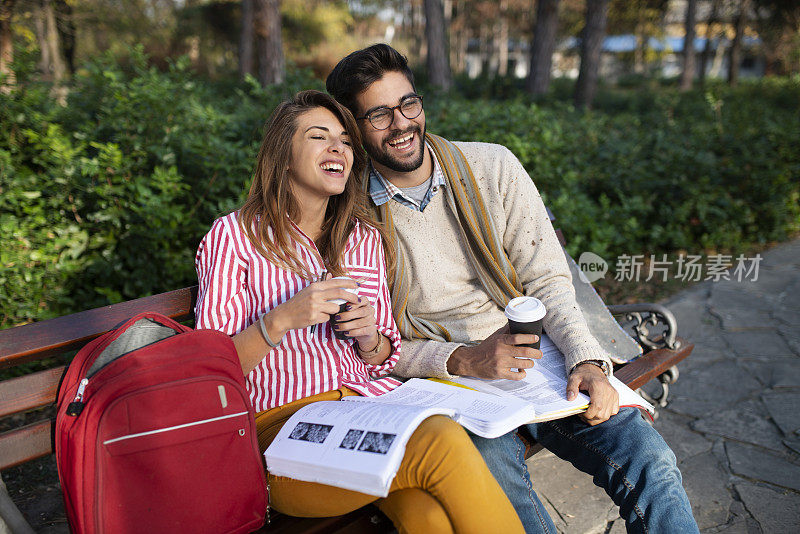 一对快乐的年轻夫妇在公园长椅上放松，他们学习和花他们的狗一天