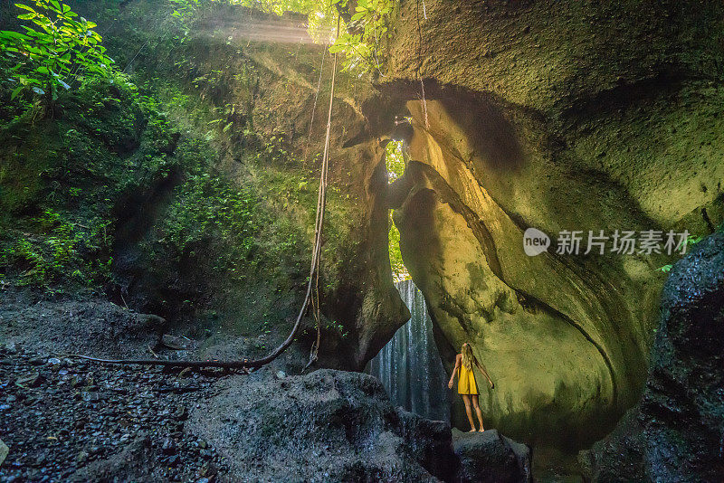 穿着黄色衣服的女孩站在热带雨林的洞穴里，仰望着从岩石上射下来的壮观的阳光。人们旅行的奇妙欲望自然的概念