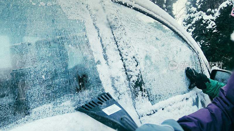 女司机刮着白雪覆盖的车窗