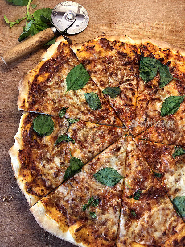 新烤的自制披萨放在用披萨刀切成三角形的木桌上，意大利那不勒斯玛格丽塔披萨薄而脆，上面点缀着金色的马苏里拉奶酪，丰富的番茄酱，意大利香草和新鲜的枯萎罗勒叶