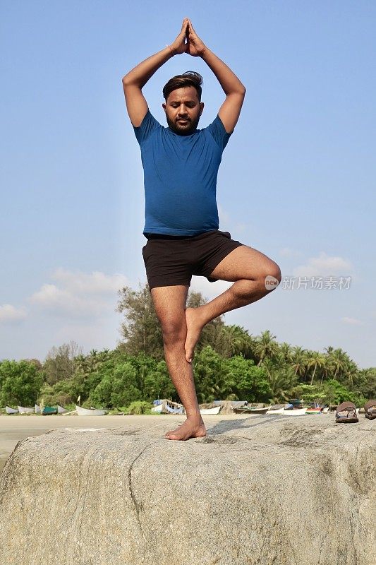 印度人在岩石上练习树姿势(Vrksasana)瑜伽姿势，水的边缘，帕洛伦海滩，果阿，印度