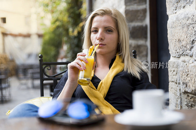 一个年轻漂亮的女人在街边小酒馆喝果汁。