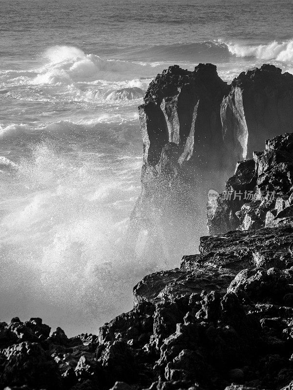 灰度照片的巨浪击中海岸上的大岩石与水飞溅和浪花