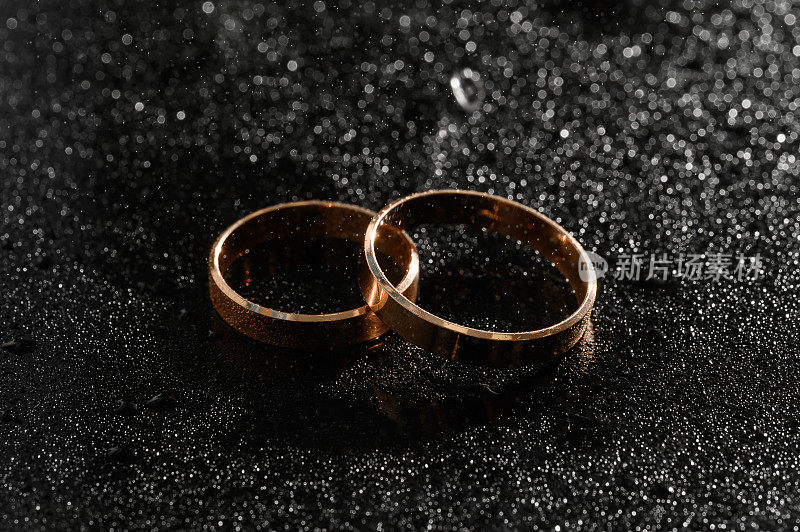 新婚夫妇的金婚戒指，黑色背景上有水滴。珠宝