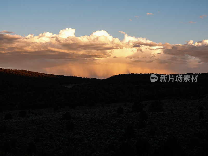 远处明亮的橙色暴风云笼罩着黑暗的沙漠山谷