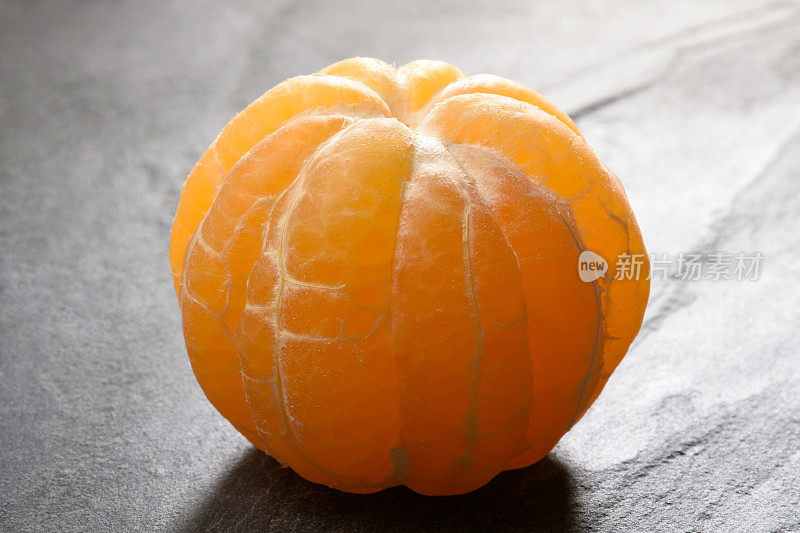 橘子，在灰色花岗岩的背景上，一整只剥了皮的橘子
