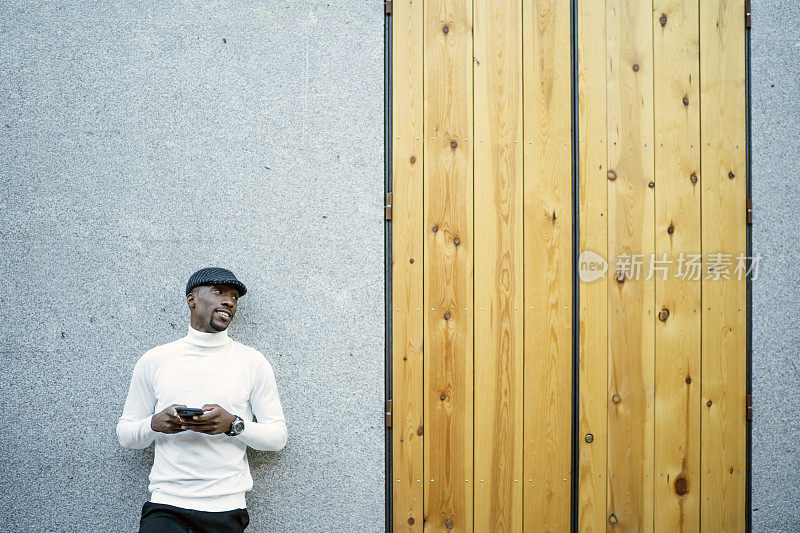 一个戴着帽子和高领毛衣的黑人拿着手机的特写镜头