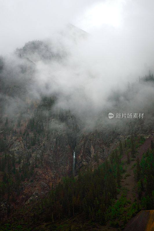 垂直低角度的小瀑布落在大山坡上，四周雾气蒙蒙，绿意葱葱