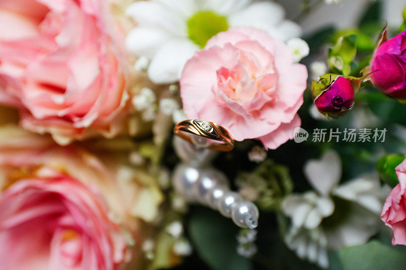 散焦一个金婚戒指。粉色的花和两枚白色背景的金婚戒。玫瑰上的结婚戒指。焦距模糊