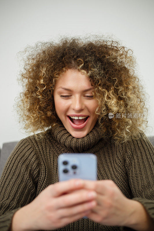 兴奋的年轻女子与智能手机。快乐的白人女性在手机社交媒体应用程序上阅读消息的肖像