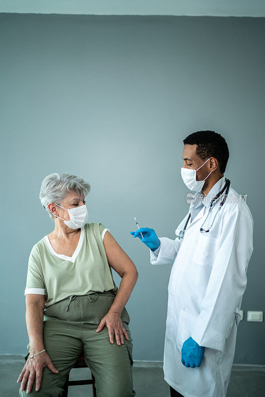 医生为一位戴着防护口罩的老年妇女接种疫苗