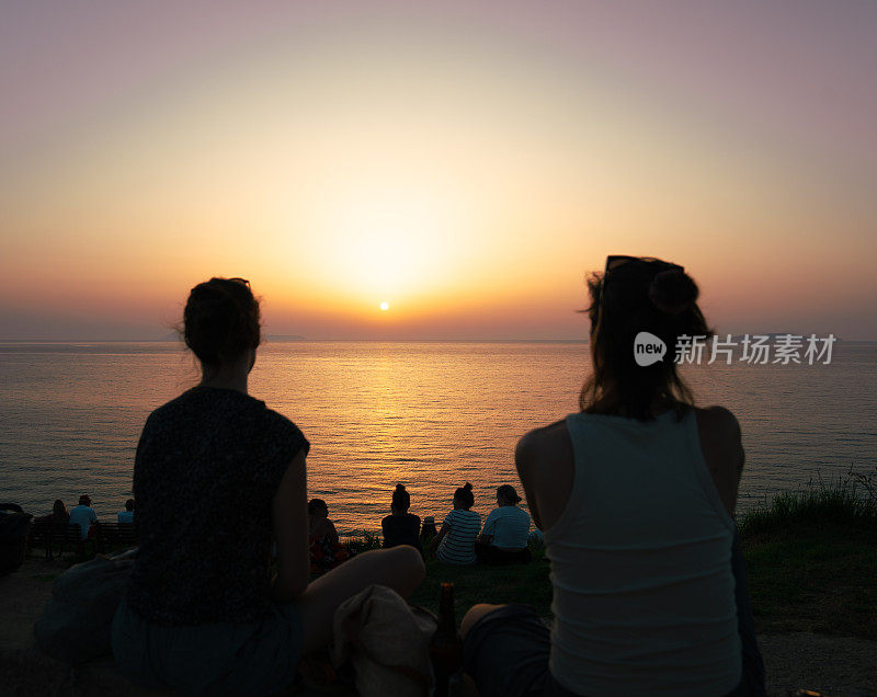 一群朋友在日落时分一起在海滩聚会，喝啤酒