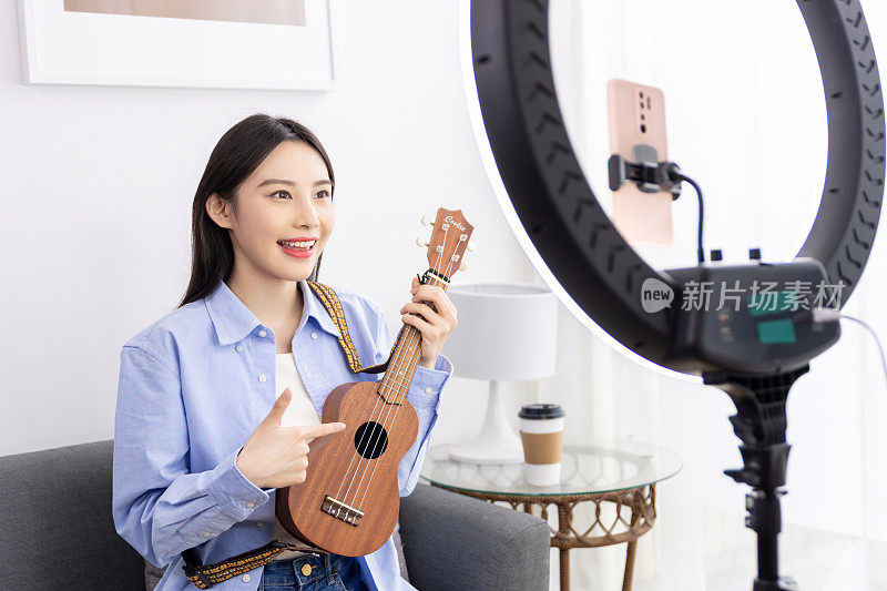 年轻女子在家里用笔记本电脑学习在线尤克里里吉他课程。学习一种乐器。