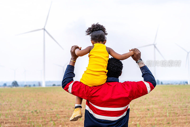 非洲黑人工程师父亲抱着他的女儿在他的怀里，在风力涡轮机非常自由。环境工程，可再生能源，热爱自然，热爱家庭的理念
