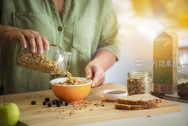 一名妇女在碗里加入什锦麦片，这是一顿健康的饭