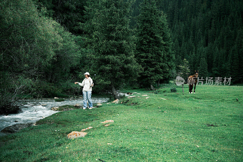 女游客在美丽的山谷中与吃草的马一起展示自己